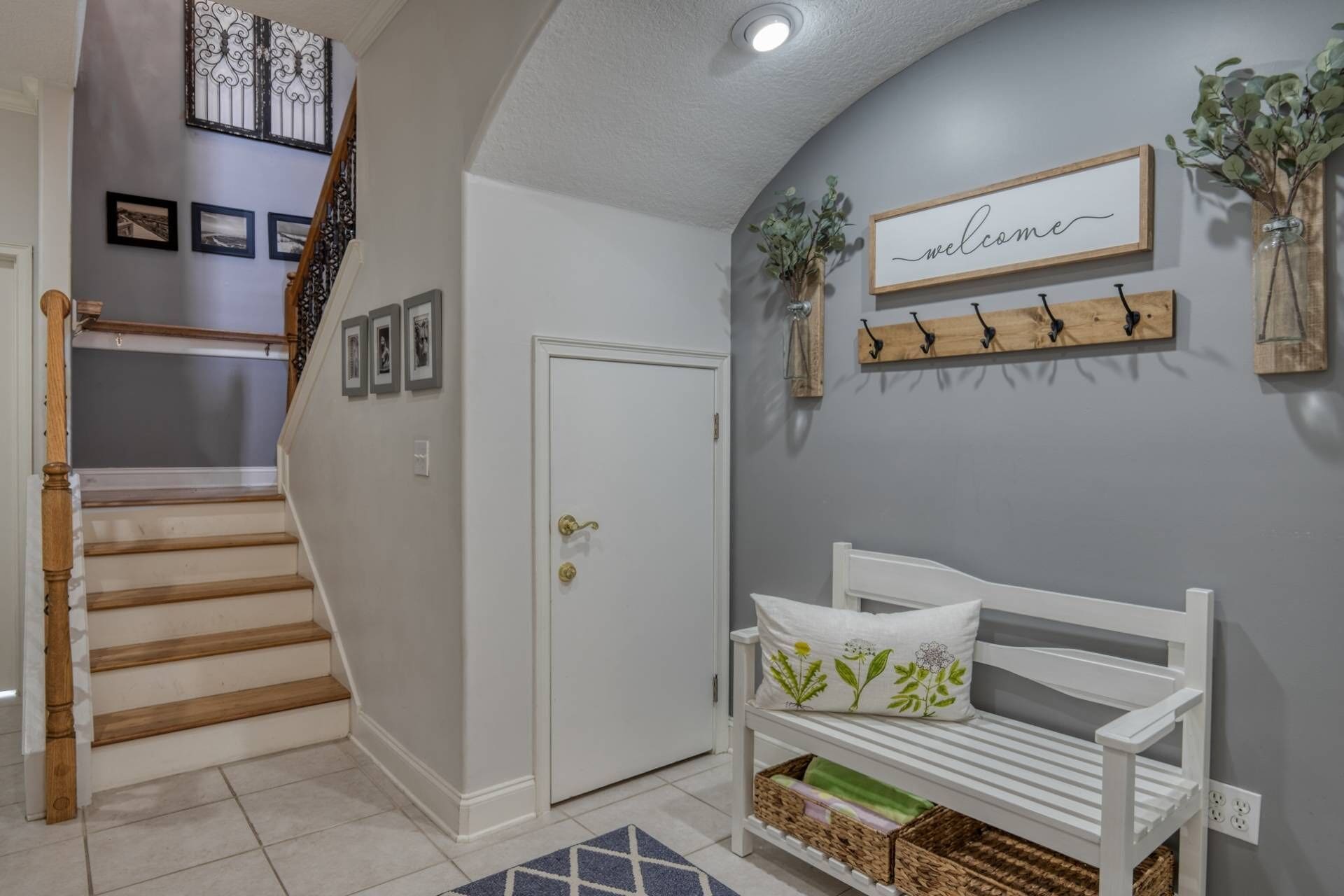A staircase with a wooden handrail, a white door, a bench with a cushion, and a 'welcome' sign on the wall.