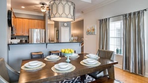A dining area with a wooden table set for six, a modern chandelier, and a view of the kitchen and living room. - Montego Bay (St. Augustine)