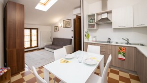 A modern kitchen with white cabinets, a dining area with a white table, and a gray sofa. - Casa Marisa (Toscolano Maderno)