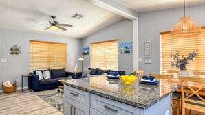 A modern kitchen with a granite countertop, a dining area with wooden chairs, and a ceiling fan. - Surf Perch - 10th St (St. Augustine)
