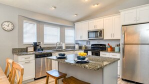 A modern kitchen with white cabinets, stainless steel appliances, a granite countertop, and a clock on the wall. - Surf Perch - 10th St (St. Augustine)