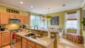 A kitchen with wooden cabinets, a stainless steel microwave, a stove, and a sink. - Bay Bridge Beach Boho (St. Augustine)