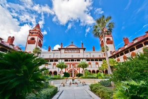A large, historic building with two prominent towers and a central dome, surrounded by lush greenery and a paved courtyard. - Bay Bridge Beach Boho (St. Augustine)