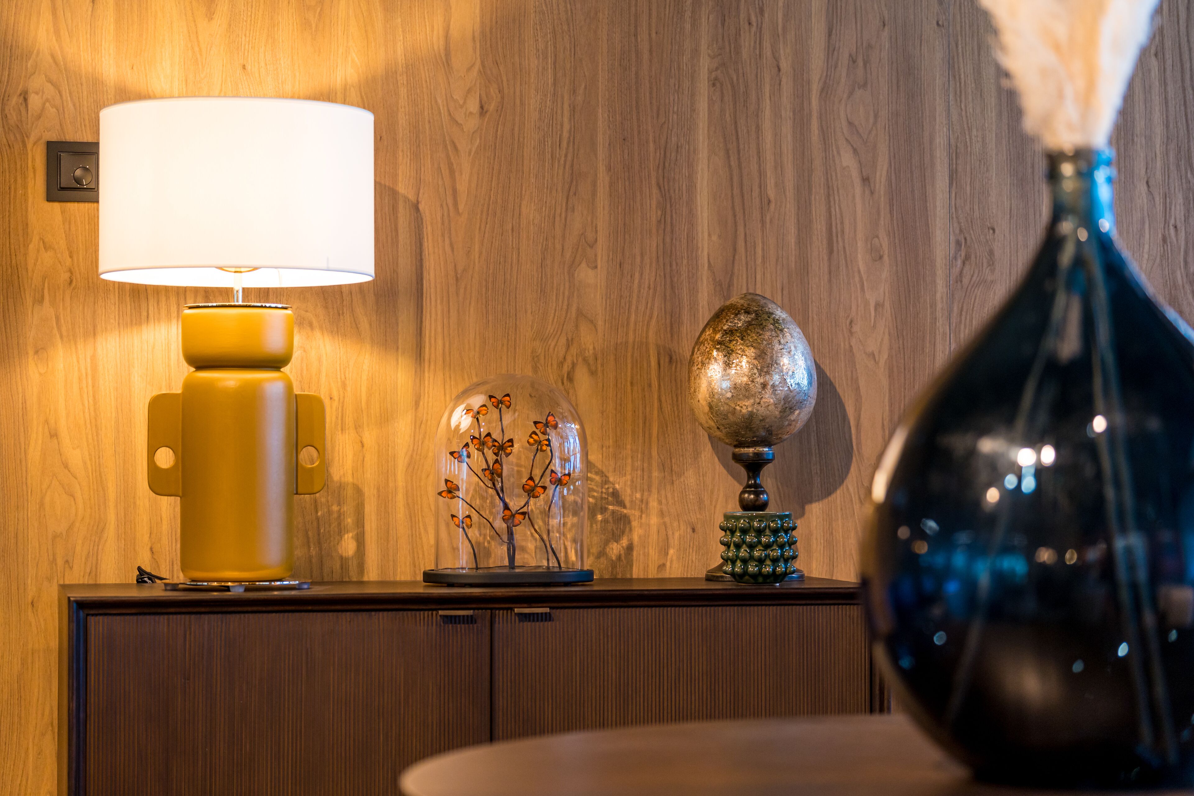 Eine Holzwand mit einer Lampe, einem Globus und einer Vase auf einem Holzkabinett.