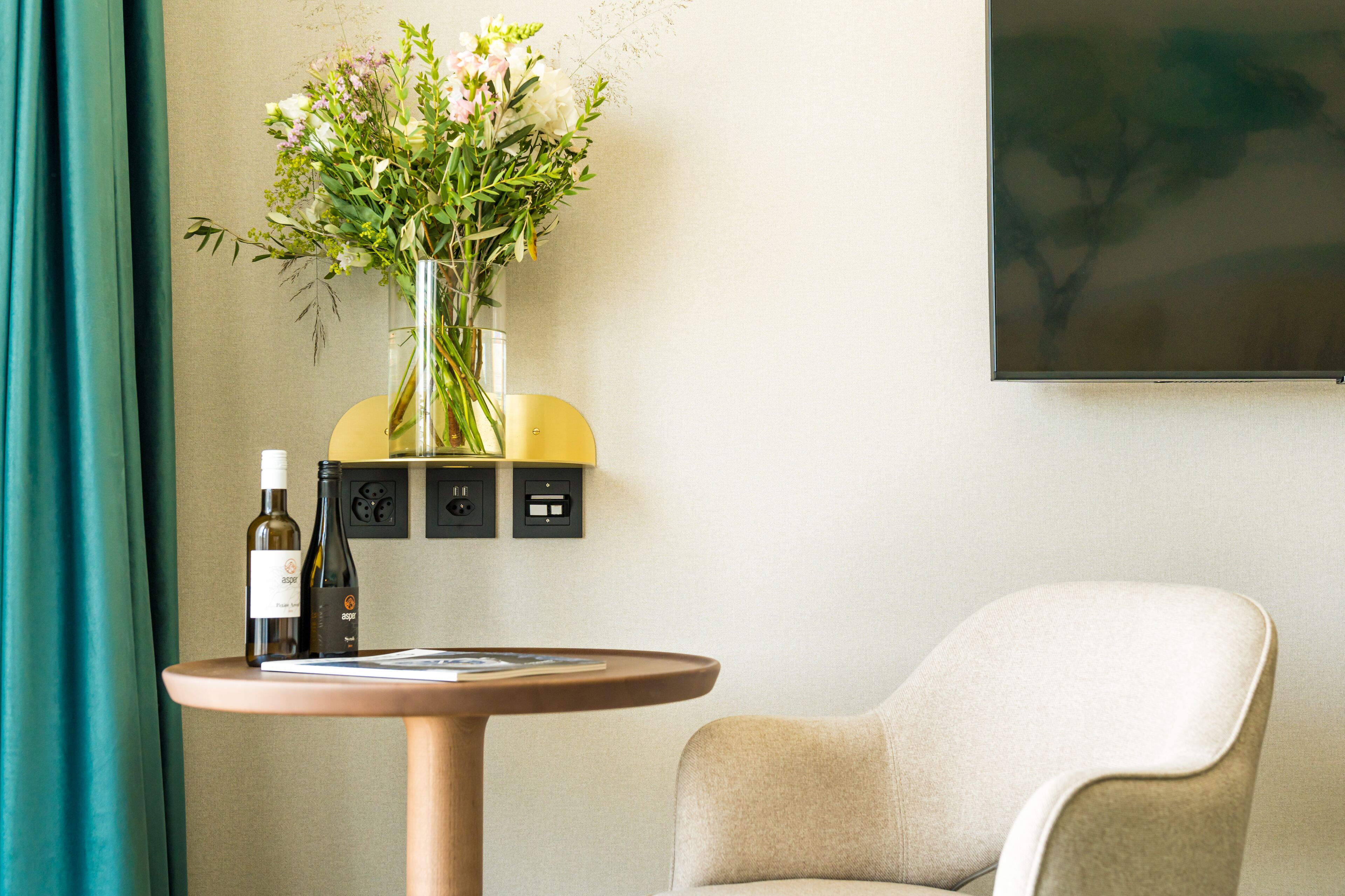 A room with a round table, a chair, a vase with flowers, and a wall-mounted power outlet.
