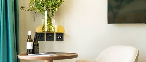 A room with a round table, a chair, a vase with flowers, and a wall-mounted power outlet.