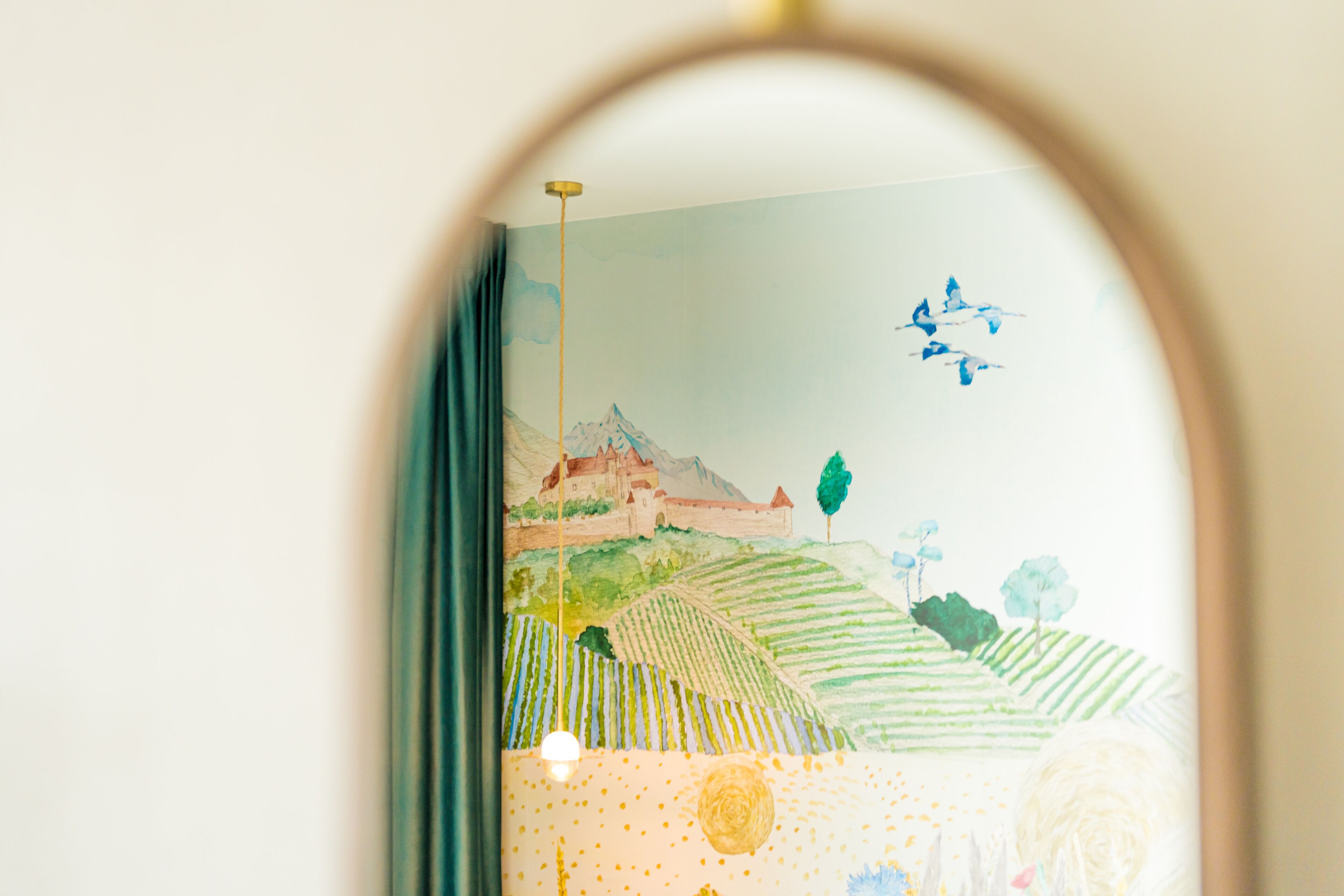 Ein Zimmer mit Wandgemälde einer Landschaft, einem Bett und einer Pendelleuchte.