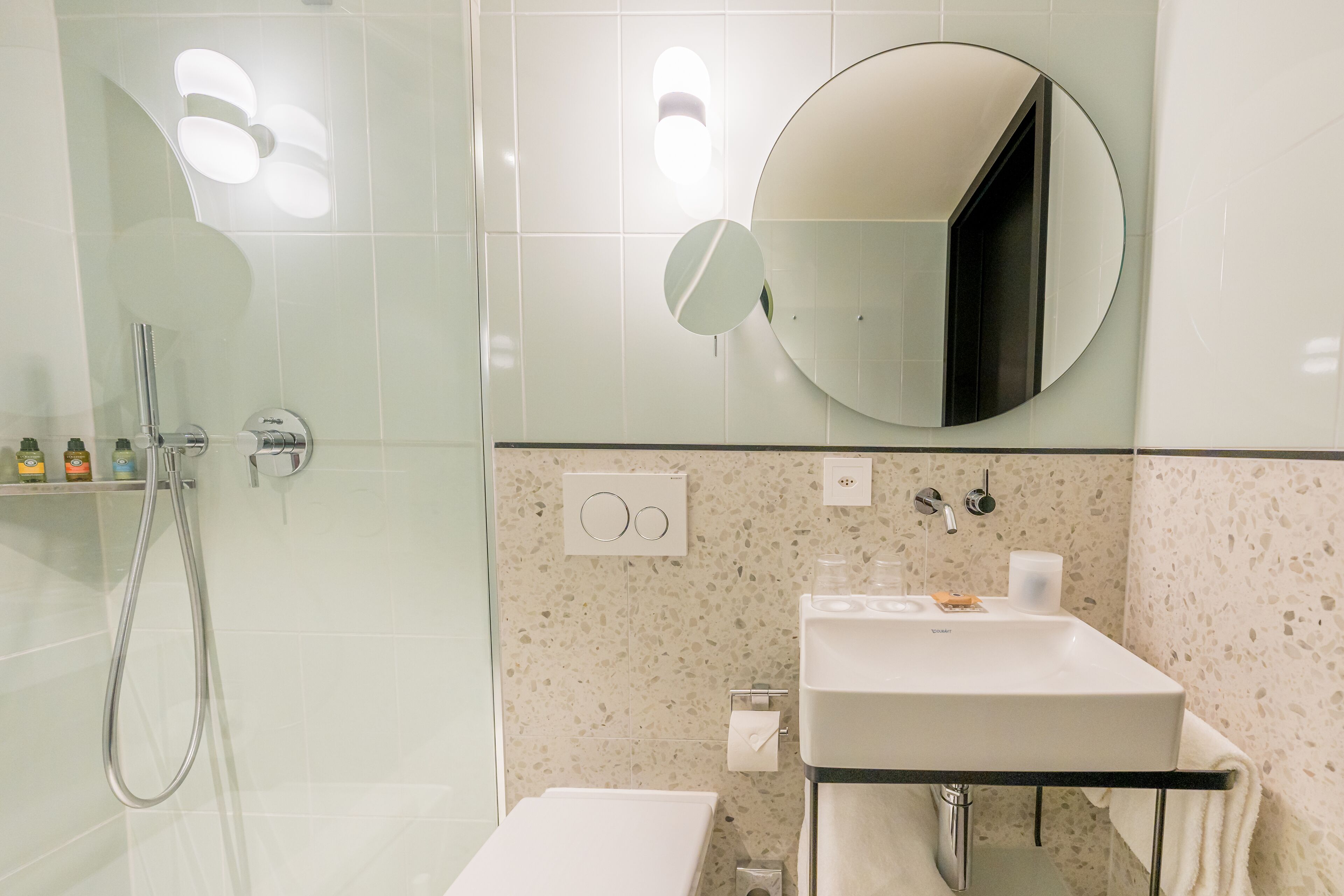 Een moderne badkamer met een douchecabine van glas, een wit wastafelmeubel en een ronde spiegel.
