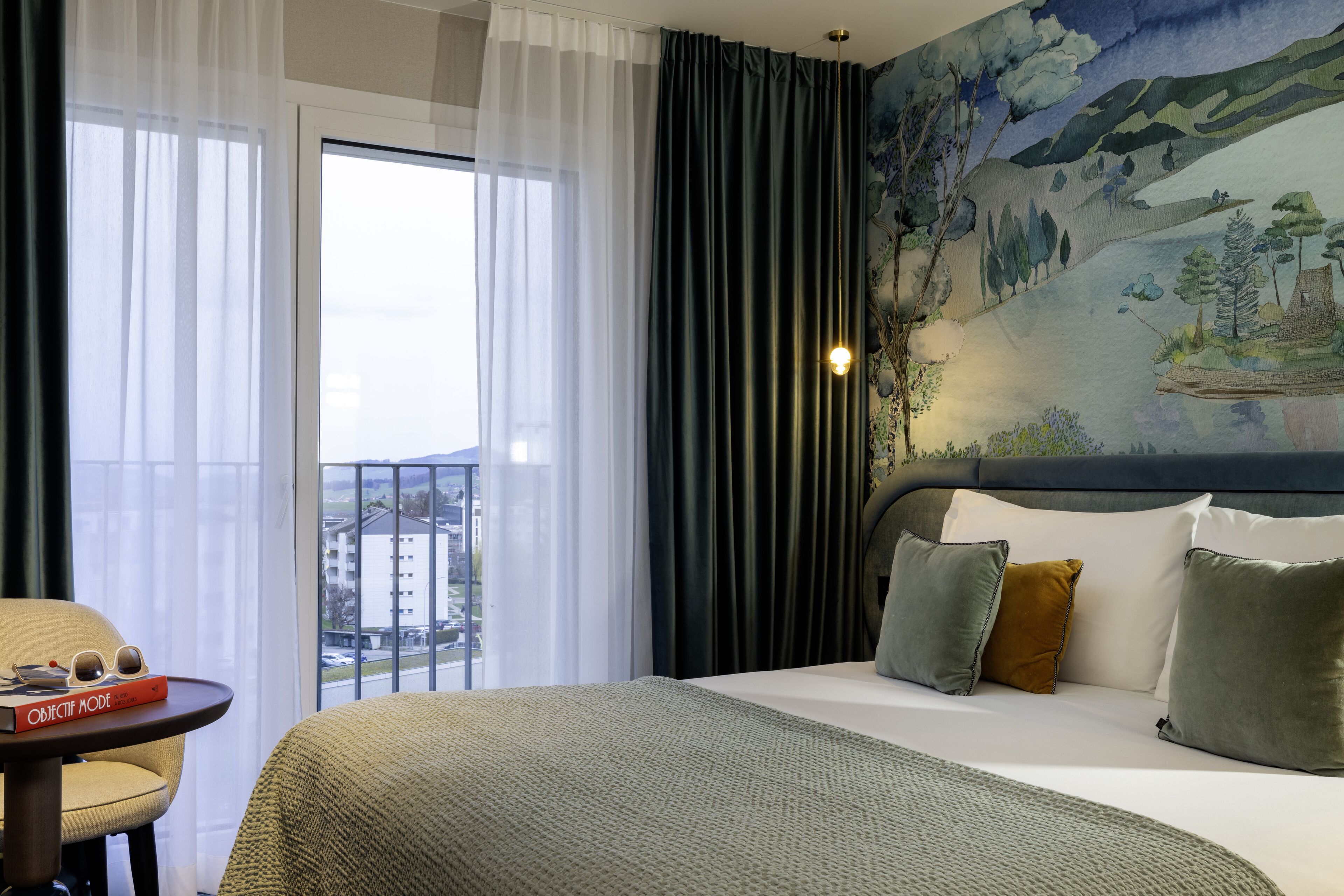 Habitación de hotel con una cama grande, vista de la ciudad a través de la ventana y un cuadro en la pared.