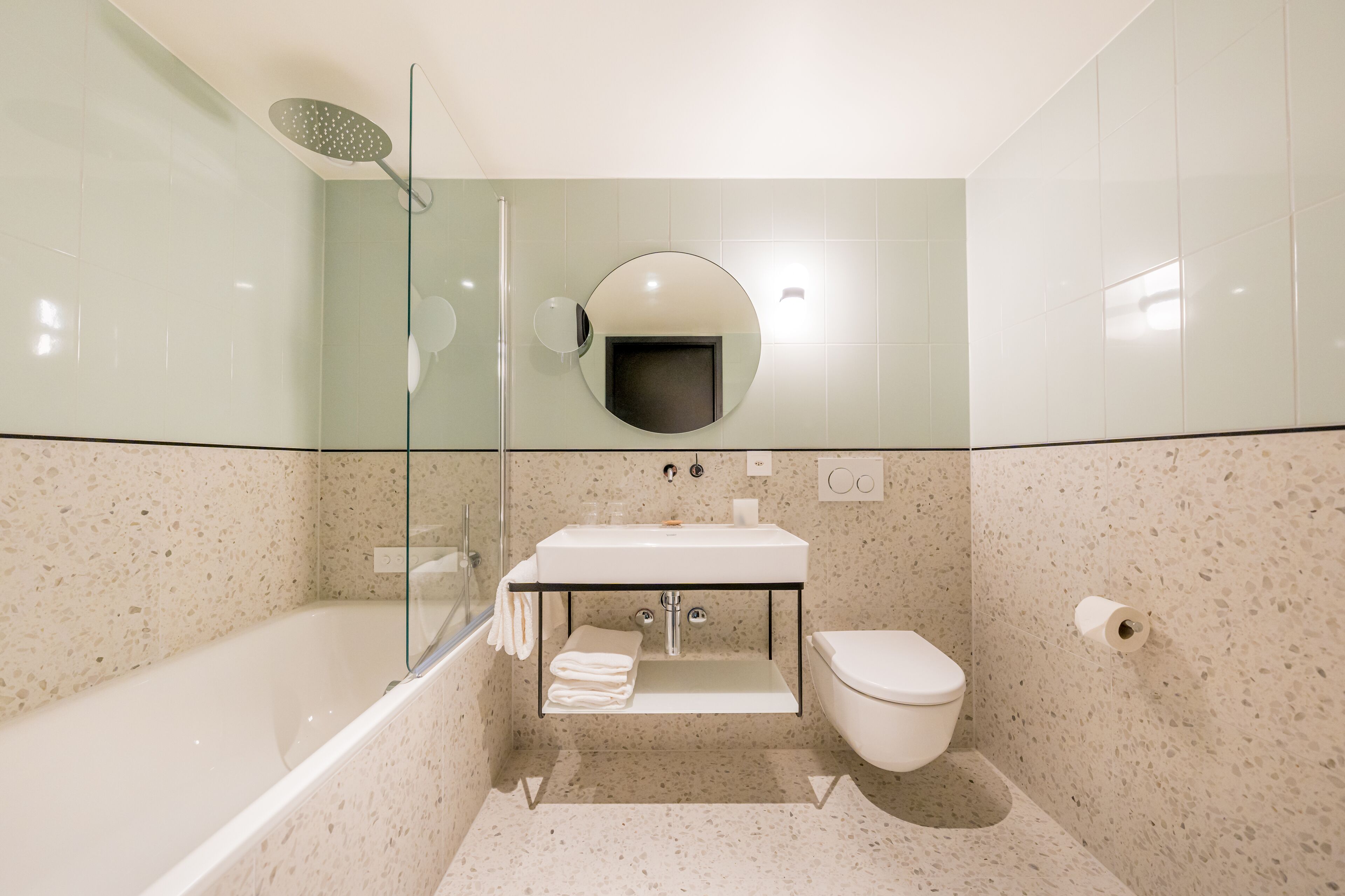 Une salle de bain moderne avec une baignoire sur pieds, une douche à parois de verre, un miroir rond et des toilettes.