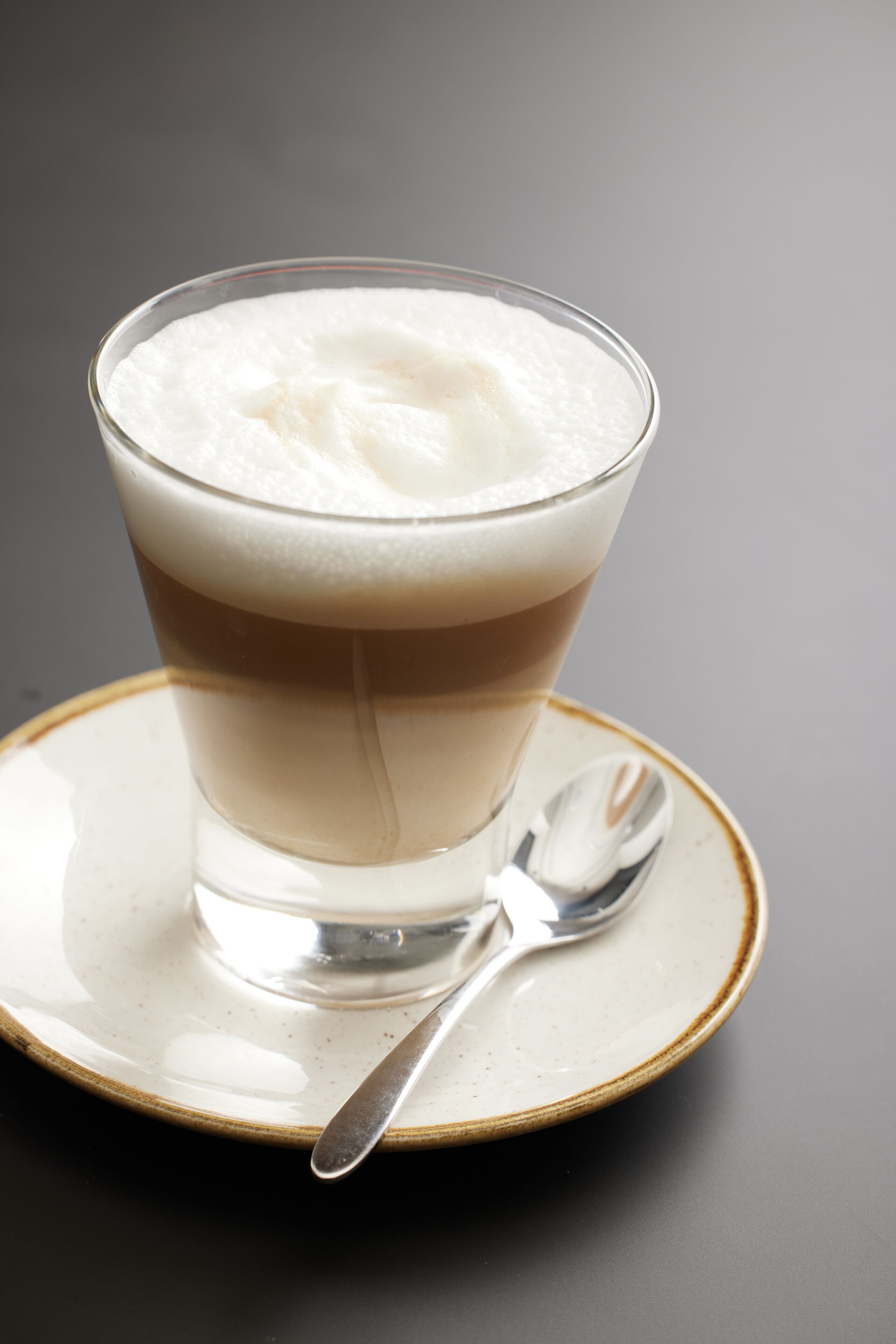 A clear glass of layered beverage with a spoon on a saucer.