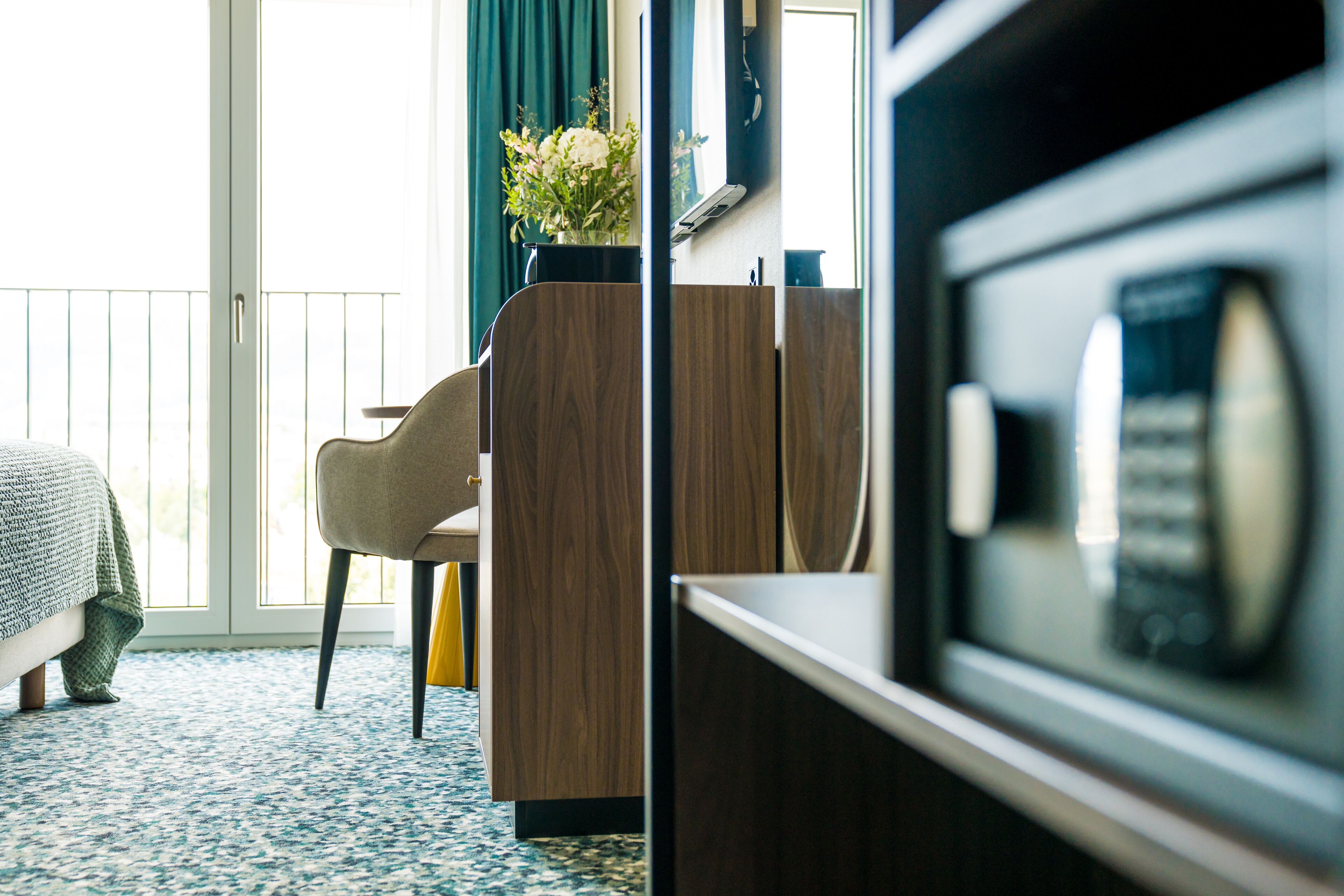 A hotel room with a bed, a desk, a chair, a TV, and a window with curtains.
