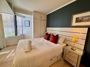 A modern bedroom with a large bed, a bedside table with a lamp, and a wardrobe.