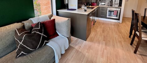 Eine moderne Küche mit einer zentralen Kochinsel, einem Essbereich mit Tisch und Stühlen und einer gemütlichen Sitzecke mit Sofa und Kissen.
