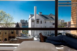 Habitación con una ventana grande que da a un paisaje urbano, una cama y vista de un edificio alto con una chimenea.