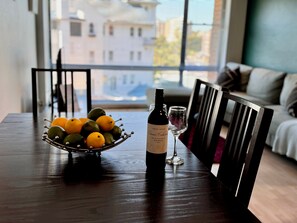 A dining table with a bottle of wine, a glass, and a bowl of fruit.