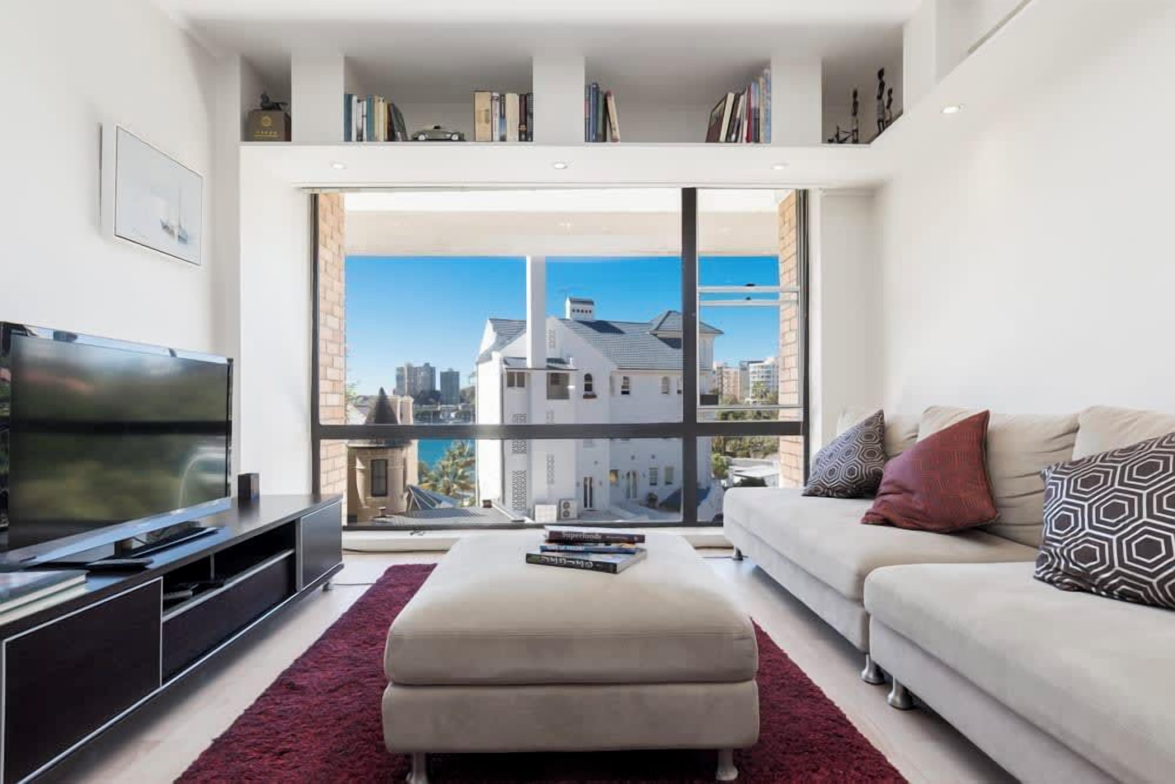 A modern living room with a large TV, a sofa, a coffee table, and a bookshelf.