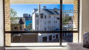 A room with a large window offering a view of a white building and a body of water.