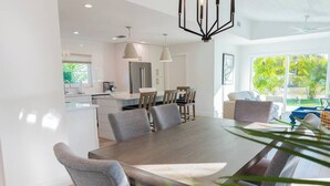 A modern kitchen with a dining area, large windows, and a view of greenery.