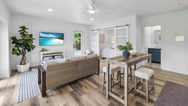 A modern living room with a sofa, a dining table, a TV, and a kitchen area.