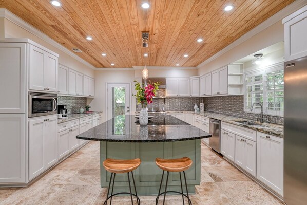 A spacious kitchen with a central island, white cabinetry, and a wooden ceiling.
