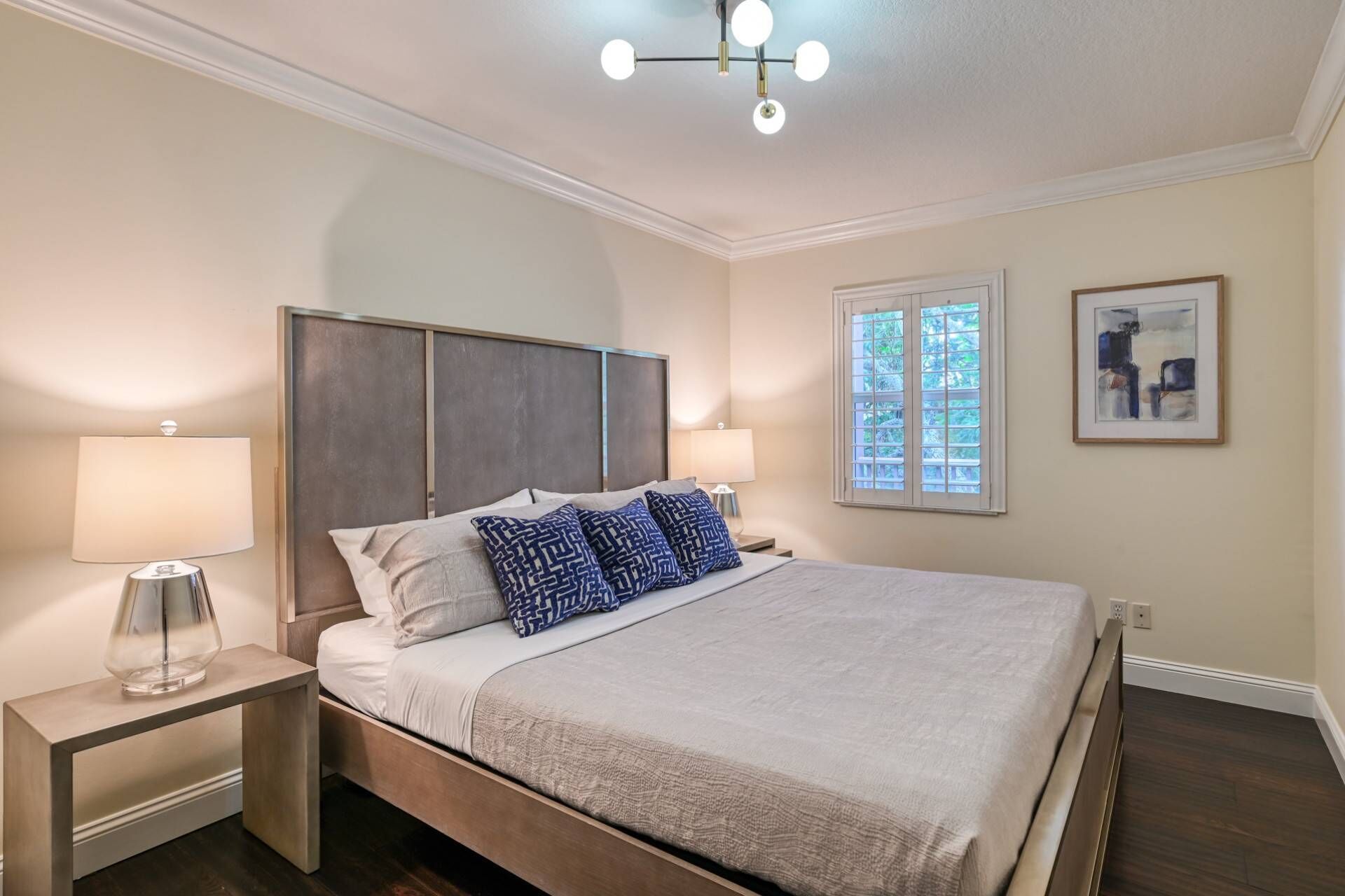 Un dormitorio ordenado con cama, lámparas de noche, una ventana con persianas y una lámpara de techo.