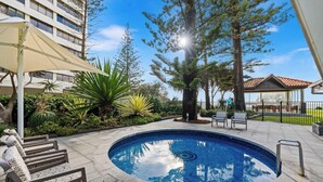 A swimming pool with a surrounding patio, a covered seating area, and a building in the background. - Surfers Paradise Beachfront Pool and Views (Surfers Paradise)