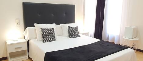 Ein ordentlich bezogenes Bett mit grau-weiß gestreifter Tagesdecke, zwei passende Kissen, ein Nachttisch mit Lampe und eine Wandleuchte.