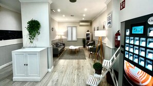 A modern waiting area with a reception desk, seating, a coffee machine, and a wall-mounted TV displaying coffee options. - ToledoRooms Palacios (Toledo)
