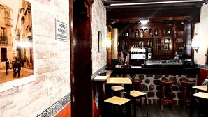 A bar area with a stone wall, wooden bar counter, and stools. There is a sign indicating a maximum occupancy of 61 persons. - ToledoRooms Palacios (Toledo)