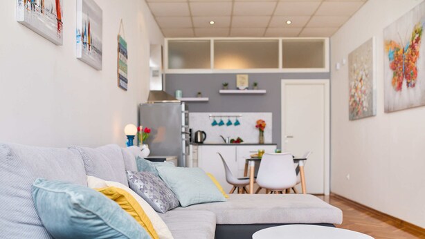 A modern living room with a grey sofa, a small white table, and a kitchen area in the background.