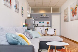 A modern living room with a grey sofa, a small white table, and a kitchen area in the background. - Apartment Aria (Dubrovnik)