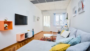 A modern living room with a sofa, a TV, a small table, and a window with curtains.