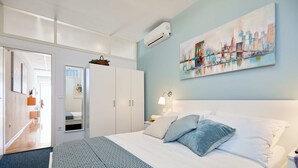 A hotel room with a bed, a painting on the wall, a wardrobe, and a door leading to another room.
