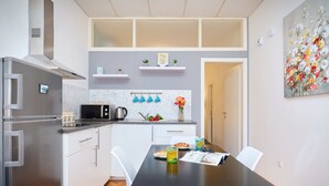 A modern kitchen with white cabinets, a stainless steel refrigerator, and a black countertop. There is a dining table with chairs and a small potted plant on the wall.