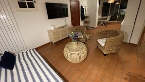 Un salon confortable avec un téléviseur, des meubles en osier et un chien allongé sur le sol.