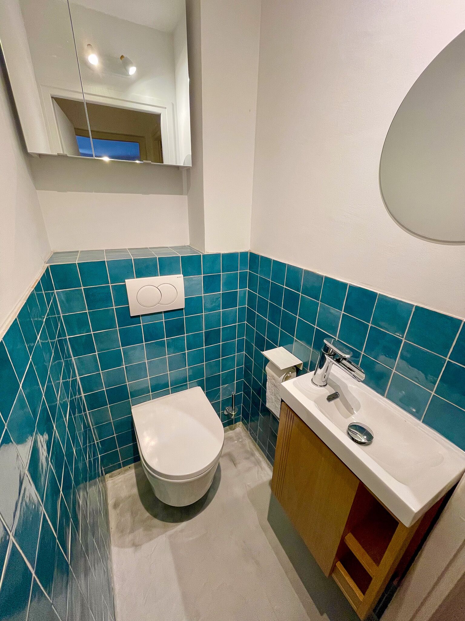 A bathroom with a white toilet, a sink with a mirror, and blue-tiled walls.