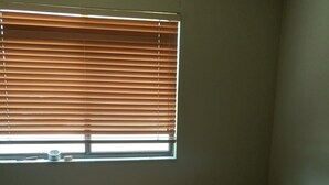 Una habitación con una cama individual, una ventana con persianas y una mesita con una taza y pañuelos.