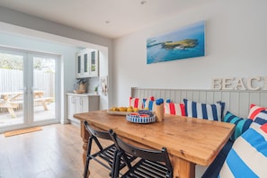A dining area with a wooden table, chairs, a bench with striped cushions, and a wall-mounted painting.