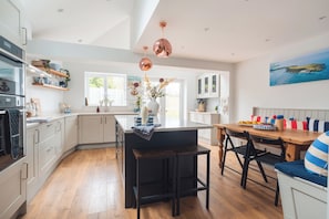 A modern kitchen with a central island, wooden flooring, and pendant lighting.