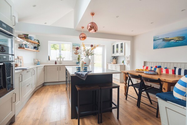 A modern kitchen with a central island, wooden flooring, and pendant lighting.