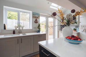 A kitchen with a window, sink, cabinets, and a bowl of fruit on the counter.