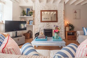 A cozy living room with a fireplace, a television, and striped cushions.