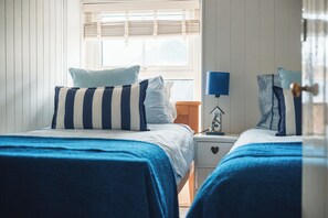 A bedroom with two beds, a nightstand, a lamp, and a window with blinds.