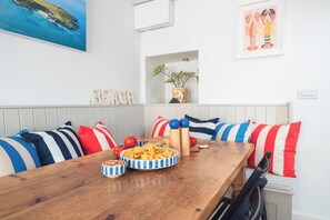 A dining area with a wooden table, striped pillows, and a wall-mounted painting of a beach.