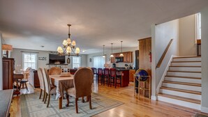Uma sala de estar espaçosa com piso de madeira, área de jantar com cadeiras e mesa, cozinha com armários de madeira e micro-ondas, e escada com decoração de globo.