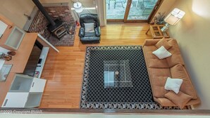 Ampla sala de estar com um sofá marrom, um tapete com padrão preto e branco, uma lareira e vista para o exterior através de uma porta de correr de vidro.