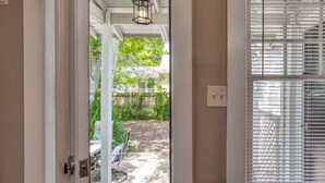 Una puerta que da a un patio con una mesa y sillas, una terraza de madera y vistas a un jardín trasero con cercas y vegetación.