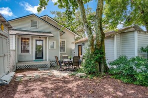 A two-story house with a porch, a dining area with outdoor furniture, and a garden with various plants. - Happy Bungalow (St. Augustine)