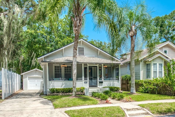 Stunning single-story home with a gabled roof and inviting front porch, set amidst beautifully manicured lawns and lush trees.